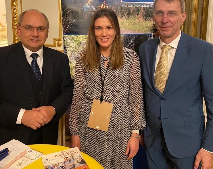 Tre persone a una presentazione turistica sulla Slovacchia in una sala dorata, accanto a un banner Travel to Slovakia e a un tavolo di opuscoli.