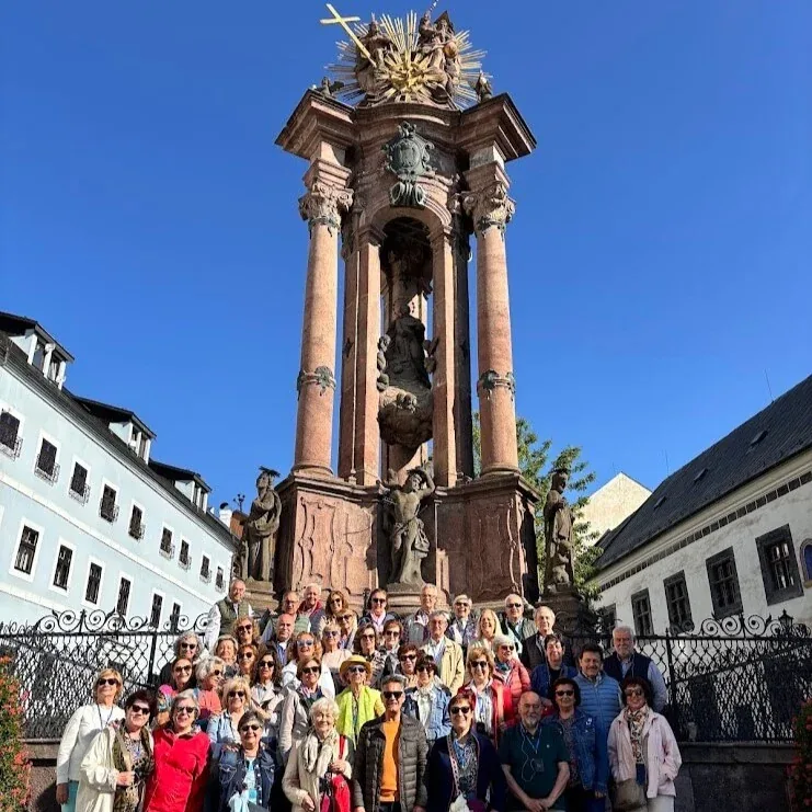 A large tour group posing in the sunshine below the baroque Holy Trinity plague column on Trinity Square in Banská Štiavnica.