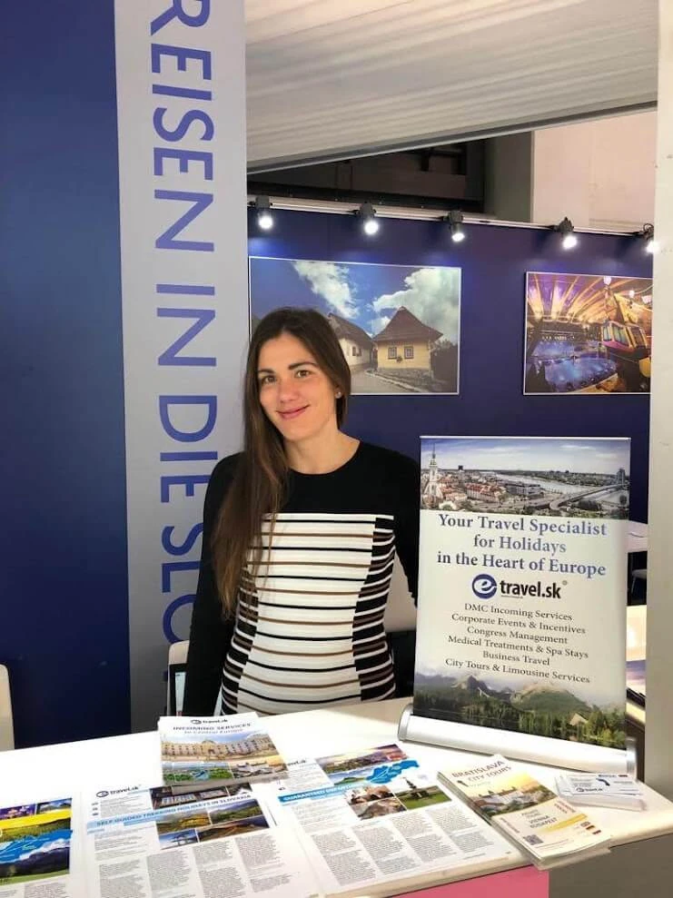 Une spécialiste du voyage d'e-travel.sk sur le stand de l'entreprise lors d'un salon professionnel du tourisme, à côté d'une bannière énumérant ses services DMC, incentive, congrès et thermalisme.