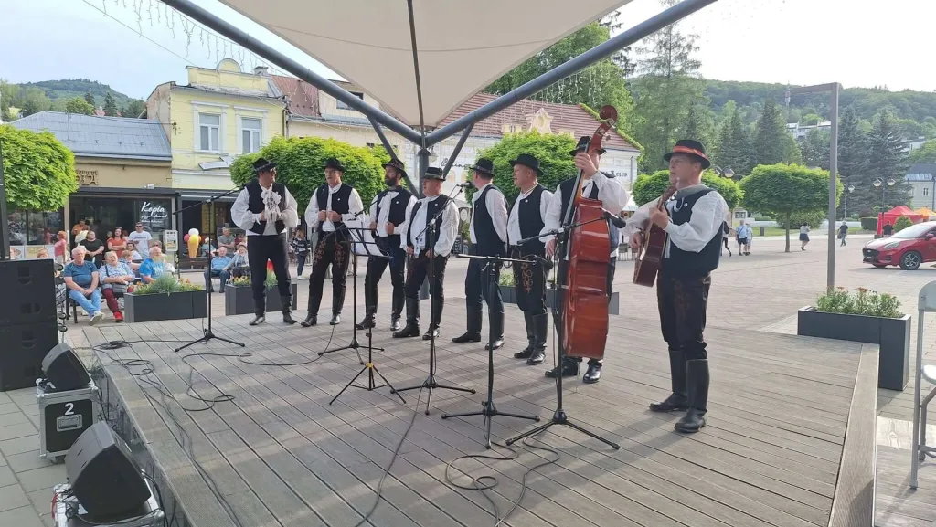 A folk group in traditional costume singing and playing on an open-air stage in Trenčianske Teplice.
