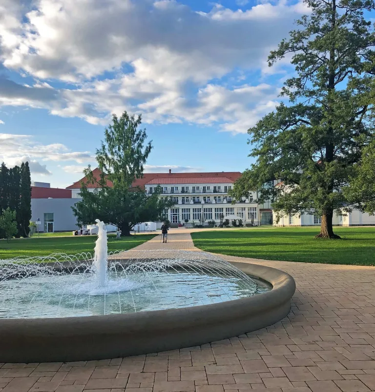A fountain in the spa park at Turčianske Teplice, with the Royal Palace hotel beyond the lawns.