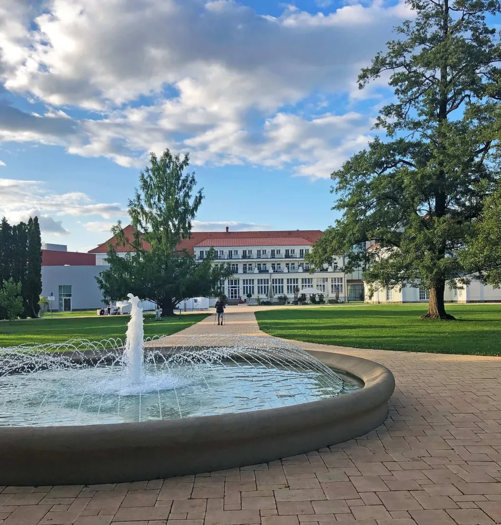 A fountain in the spa park at Turčianske Teplice, with the Royal Palace hotel beyond the lawns.