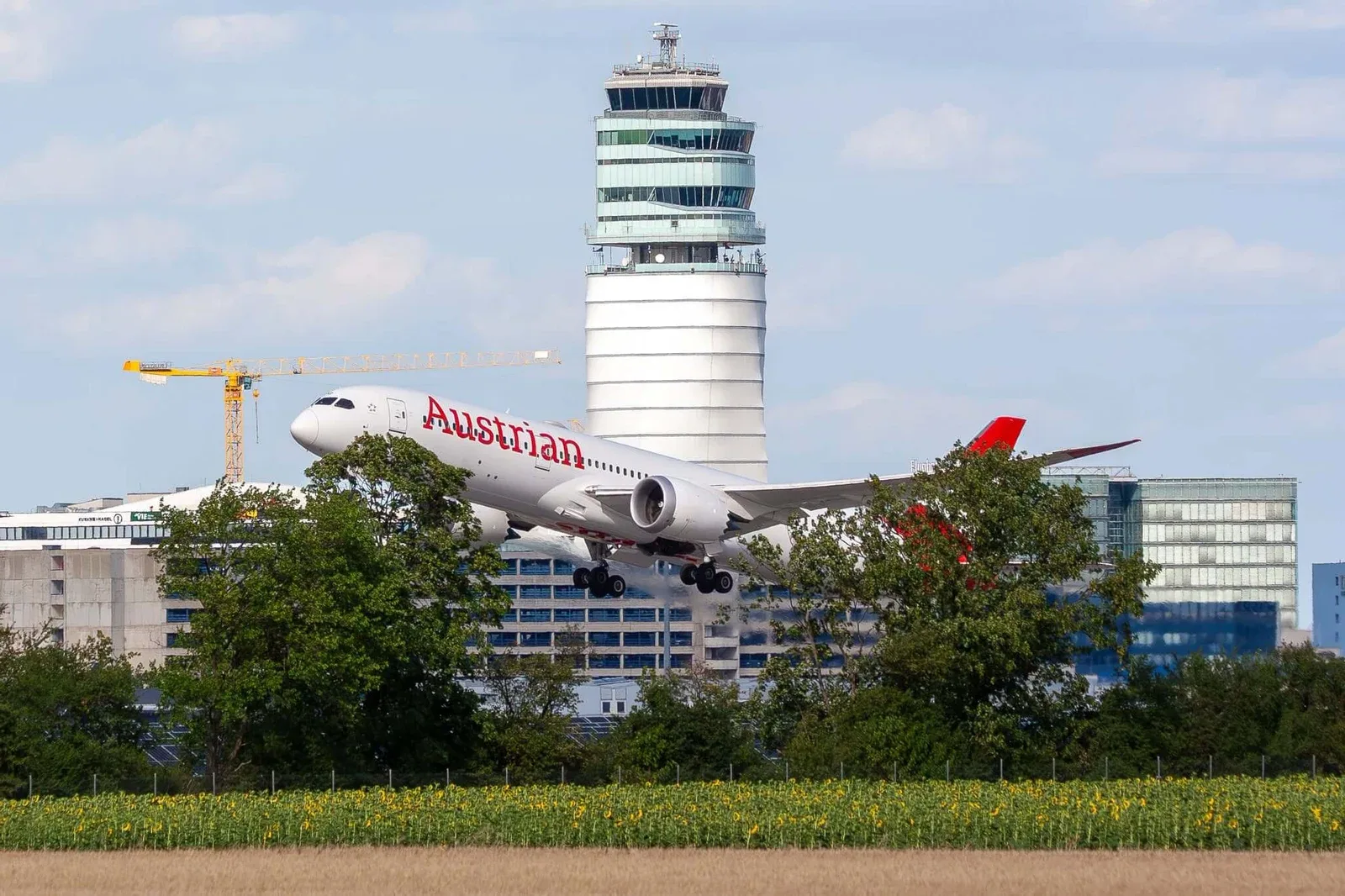 An Austrian Airlines Boeing 787 taking off at Vienna International Airport, with the airport’s control tower behind it.