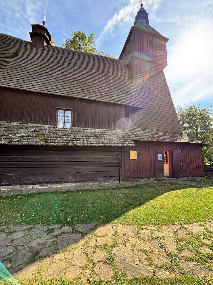 The wooden Church of St Francis of Assisi at Hervartov, its dark shingled walls and steep roof in the afternoon sun.