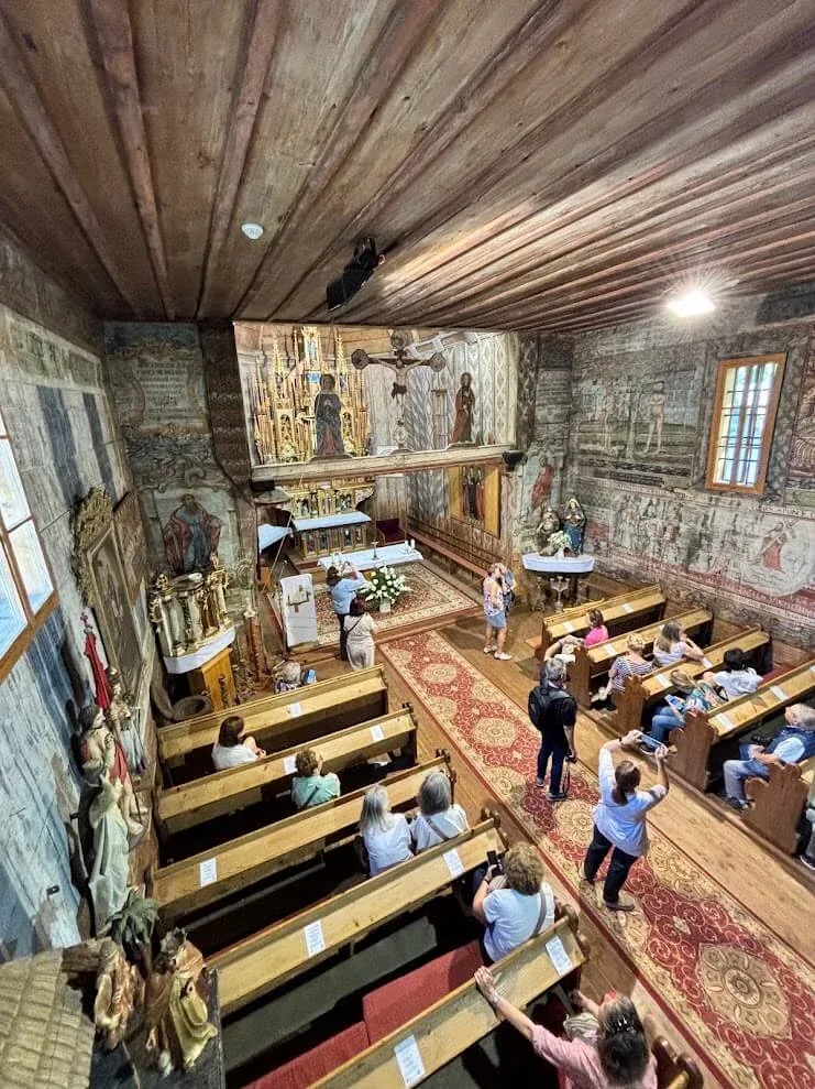 Visitors inside the wooden Church of St Francis of Assisi at Hervartov, looking at the painted walls and the carved altar.