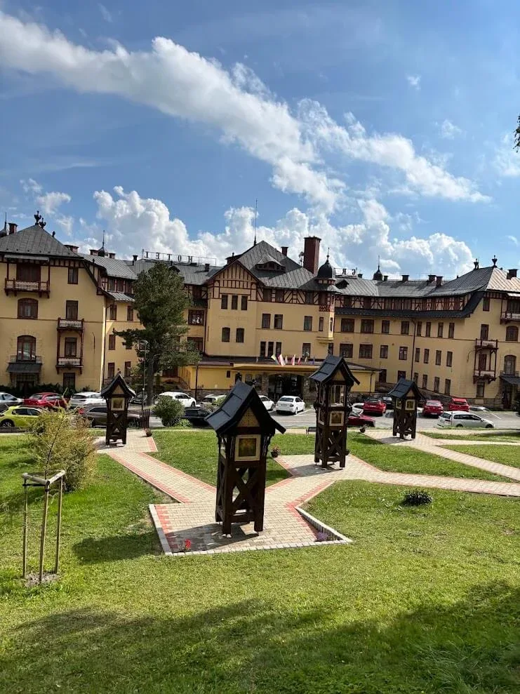 A grand historic hotel in the High Tatras, its cream and timbered facade behind a lawn set with carved wooden shrines.