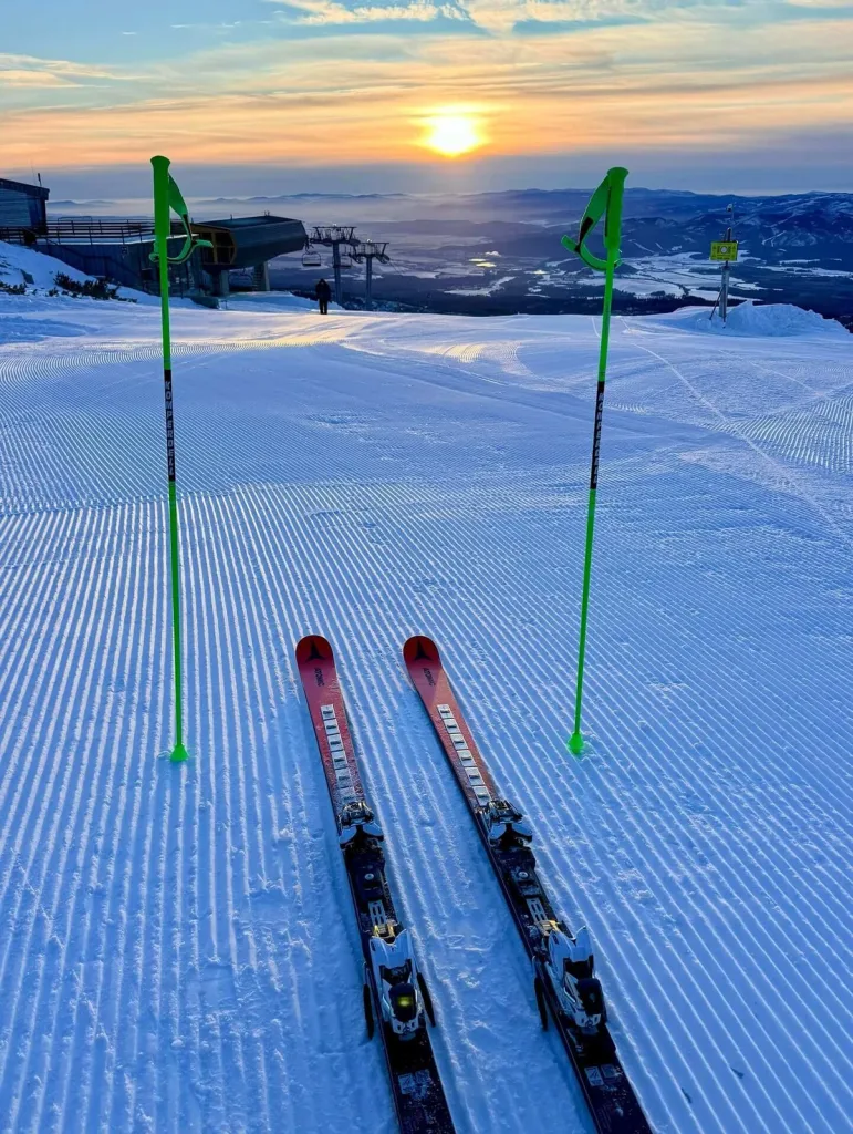 Skis and poles standing on a freshly groomed piste in the High Tatras at sunrise, with a chairlift and the valley below.
