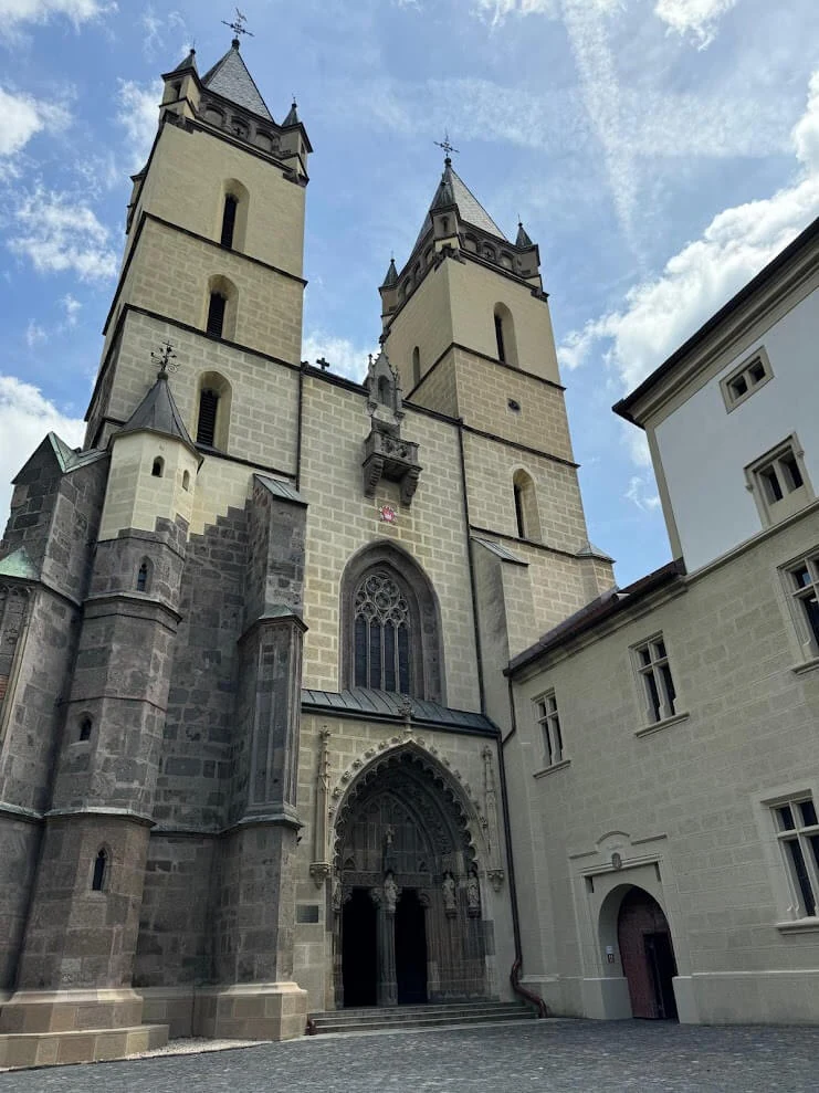 The twin-towered Gothic abbey church at Hronsky Benadik, its carved stone portal and rose window above the courtyard.