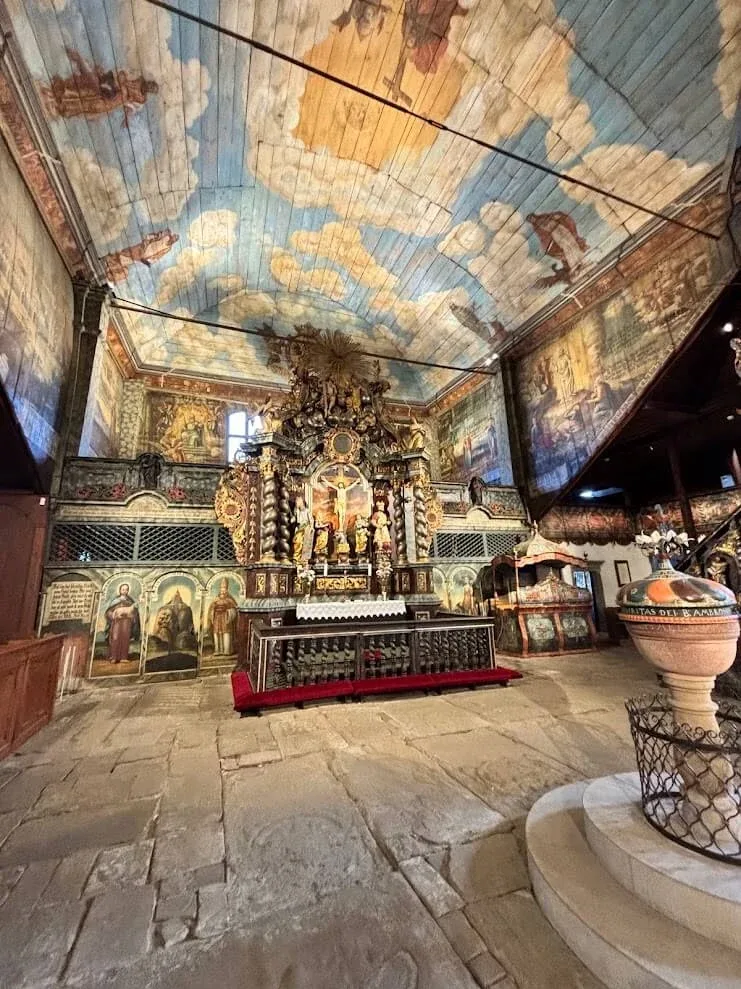 The painted interior of the wooden Articular Church in Kežmarok, its timber ceiling painted as a cloudy sky above a baroque altar.