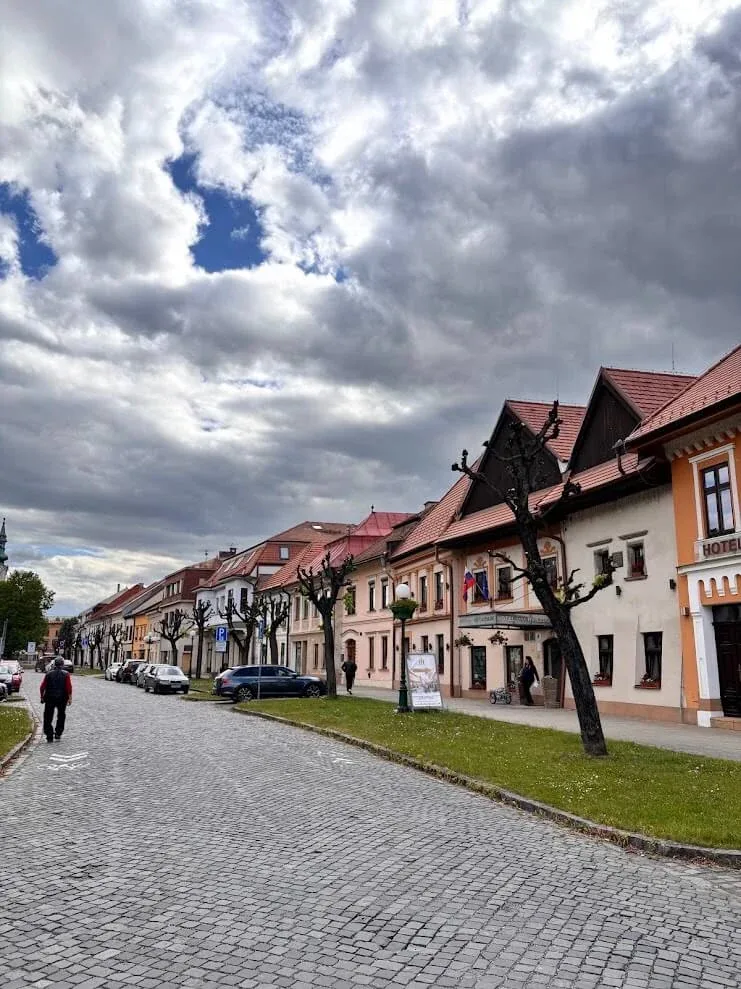 The long cobbled main street of Kežmarok, lined with gabled pastel houses under a cloudy sky.