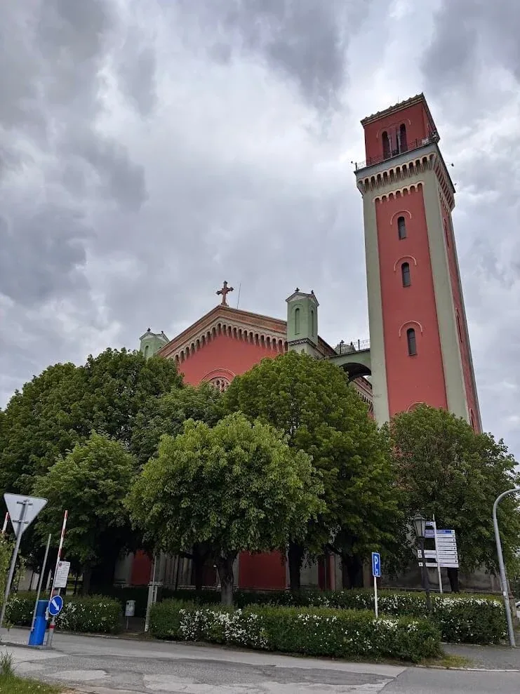 The red and green New Evangelical Church in Kežmarok with its tall corner bell tower, behind a row of lime trees.