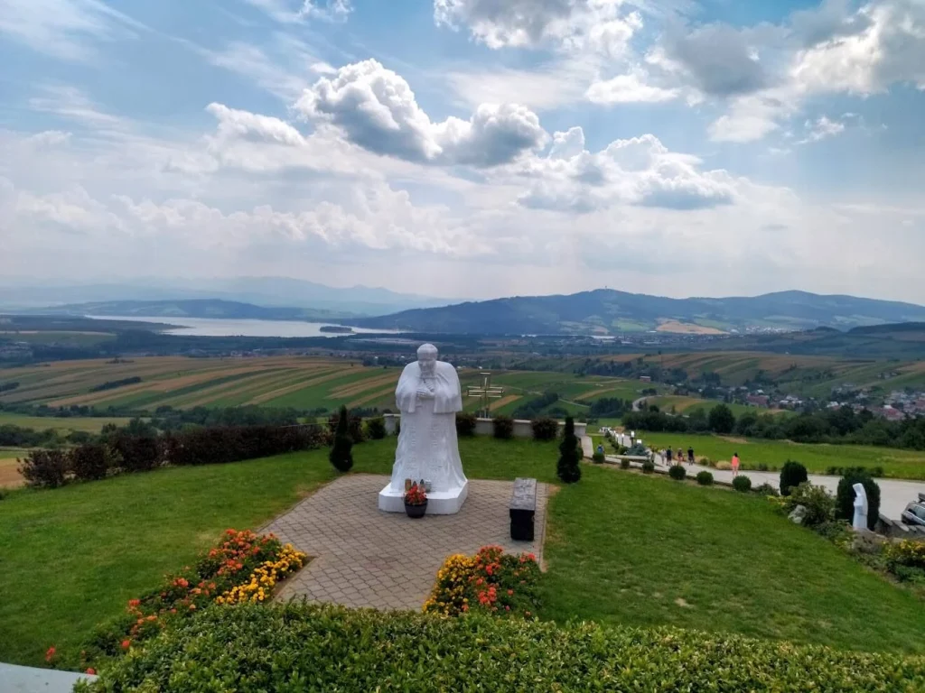 The white statue of Pope John Paul II at Klin, looking out over fields towards the Orava reservoir and the hills beyond.