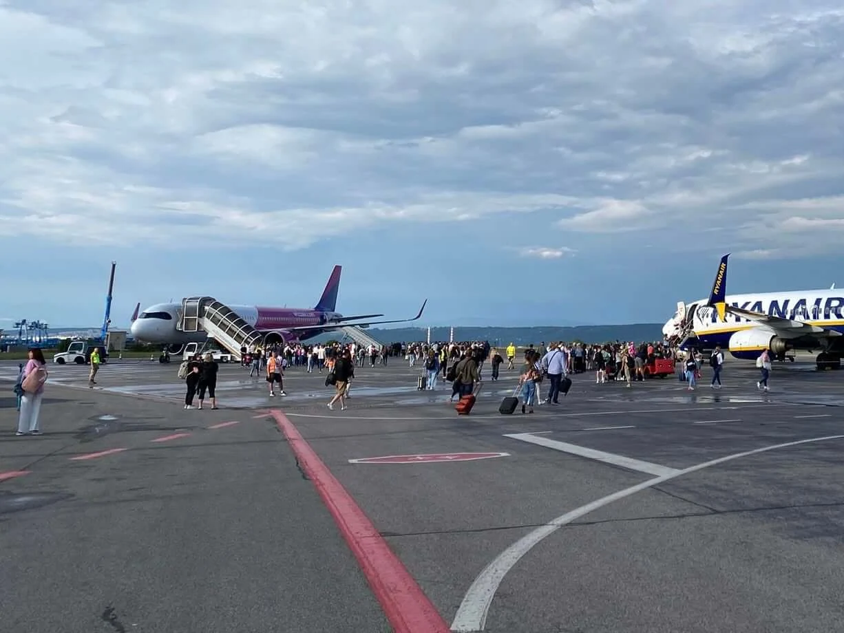 Passengers walking across the apron at Košice Airport after landing, with a Wizz Air aircraft on the left and a Ryanair aircraft on the right under an evening sky.