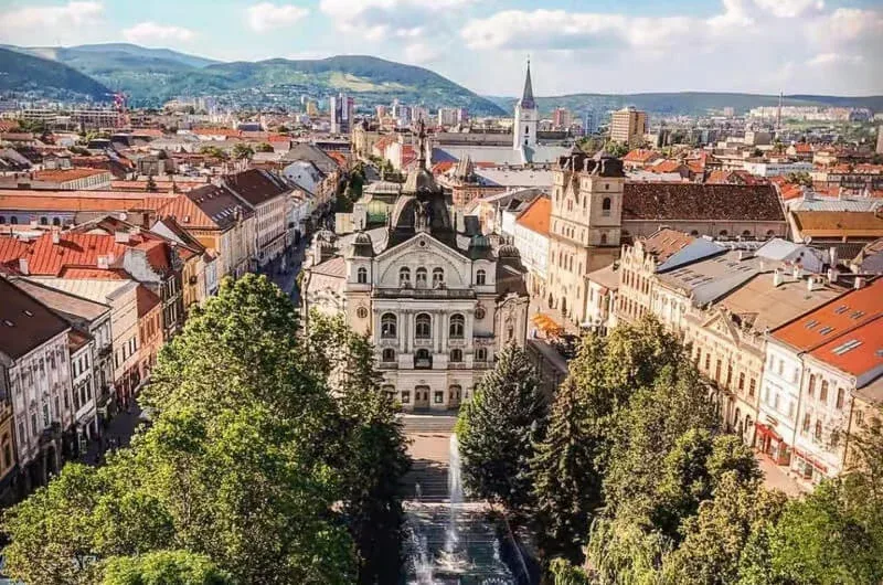 Košice's Hlavná street from above, the State Theatre and the Singing Fountain framed by trees, with the hills beyond the city.