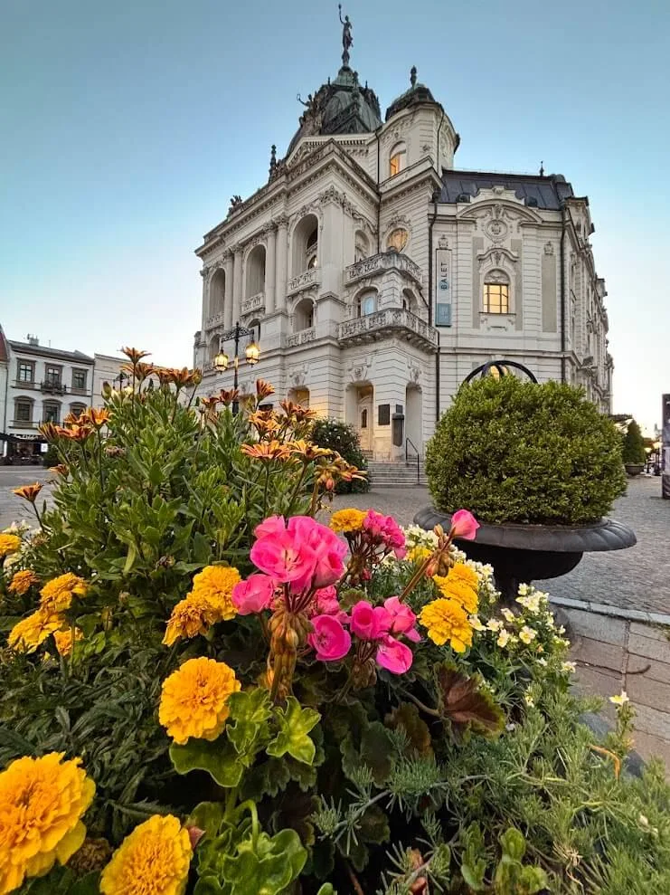 Le Théâtre d'État de Košice au crépuscule, vu au-dessus d'un parterre de fleurs sur la place principale.