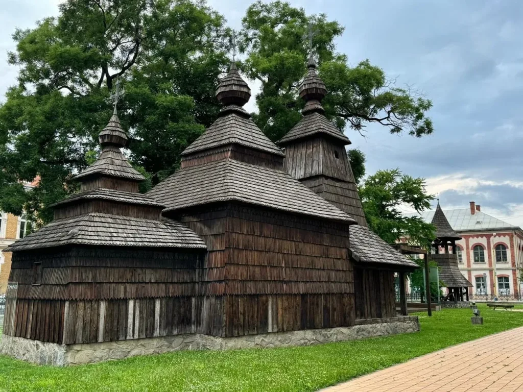 The wooden Greek Catholic church in Košice, its shingled walls and three onion domes standing under old trees.
