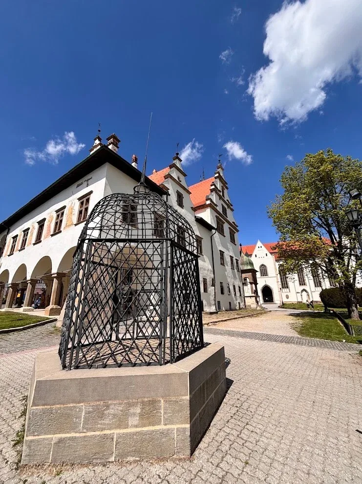 The wrought-iron cage of shame standing on the square in front of the arcaded town hall of Levoča.
