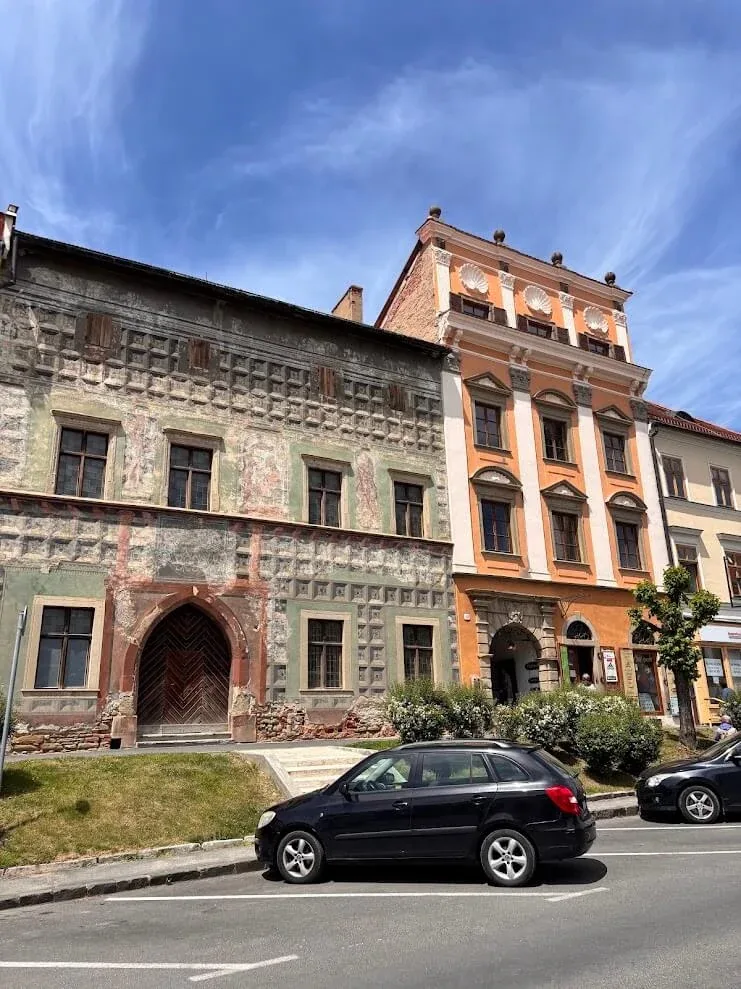 A Renaissance burgher house in Levoča with faded sgraffito decoration and a Gothic doorway, beside a bright orange neighbour.