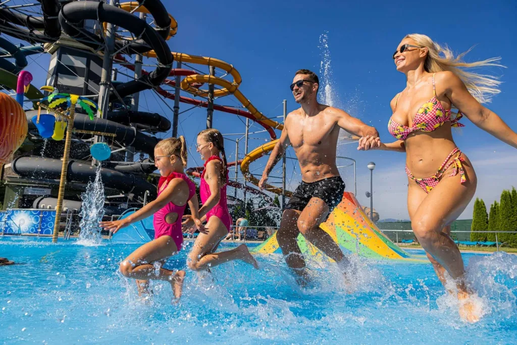 A family running into the outdoor pool of an aquapark in the Liptov region, with water slides rising behind them.