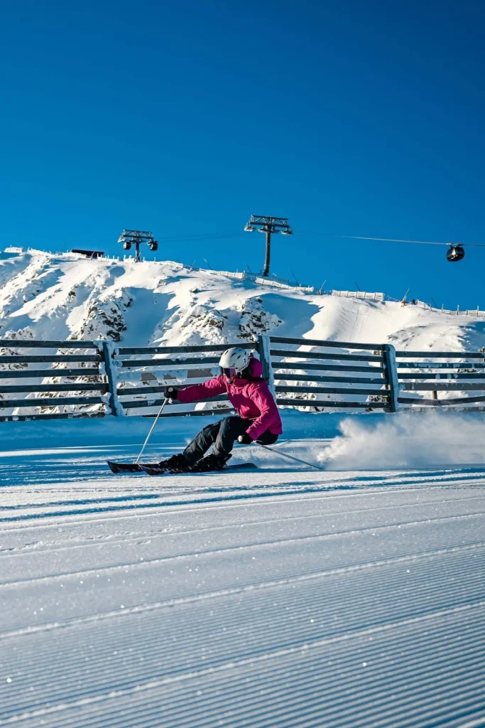 A skier in a pink jacket carving a turn on a freshly groomed piste in the Low Tatras, with a chairlift above.