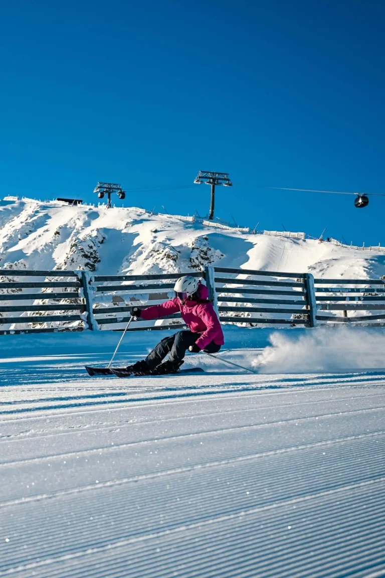 A skier in a pink jacket carving a turn on a freshly groomed piste in the Low Tatras, with a chairlift above.
