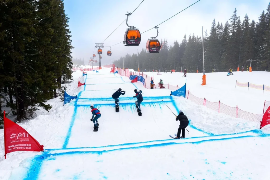 A snowboard-cross course marked out in blue on a piste in the Low Tatras, with gondola cabins passing overhead.