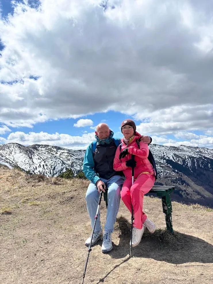 Two walkers with poles resting on a bench high on a Malá Fatra ridge, with snow still lying on the slopes behind.
