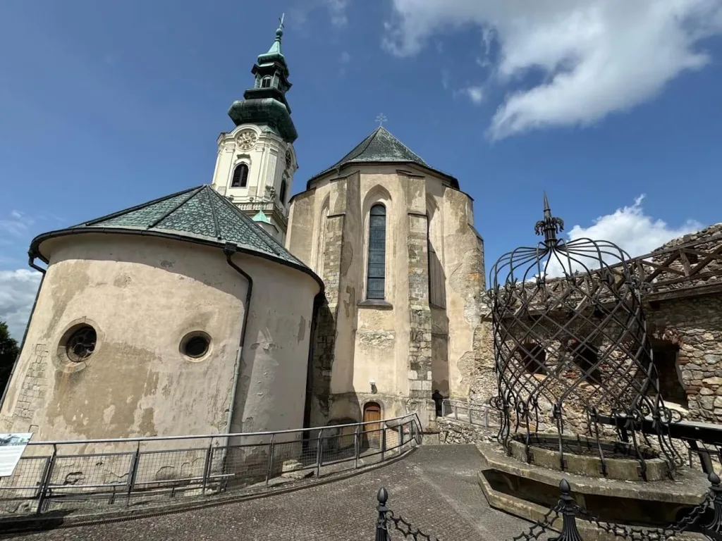 The round chapel and Gothic apse of St Emmeram's Cathedral inside Nitra Castle, with the wrought-iron cage over the castle well in the foreground.