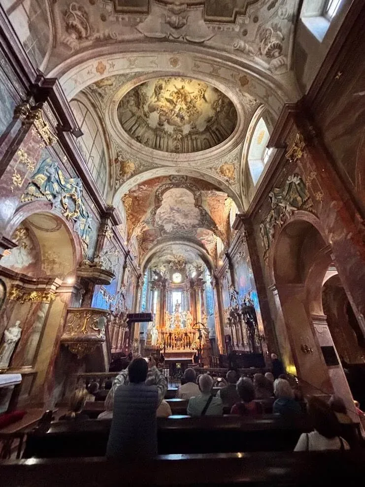 The frescoed dome and high altar of St Emmeram's Cathedral in Nitra, seen down the nave over the heads of a seated congregation.