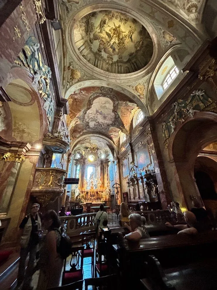 A group seated in the pews of St Emmeram's Cathedral in Nitra, beneath its frescoed baroque vault and gilded side altars.