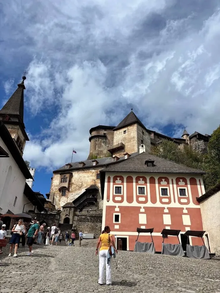The lower courtyard of Orava Castle, with its red and white painted building below the fortress rising on the rock.