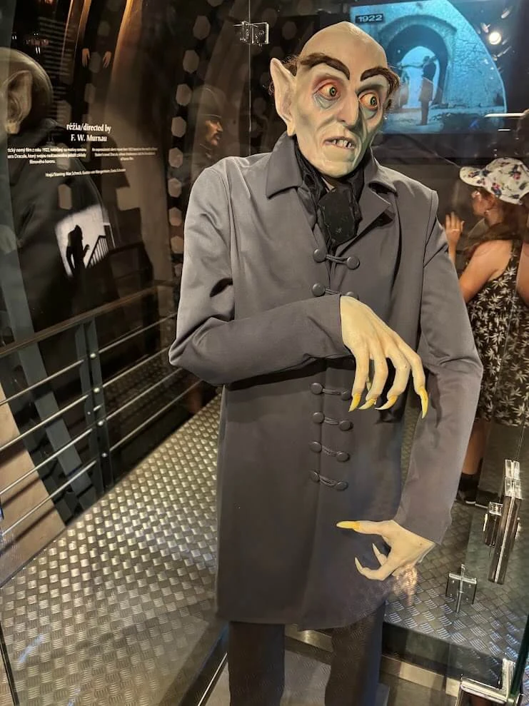 A life-size figure of Count Orlok from the 1922 film Nosferatu displayed in a glass case at Orava Castle, beside a screen showing scenes filmed there.