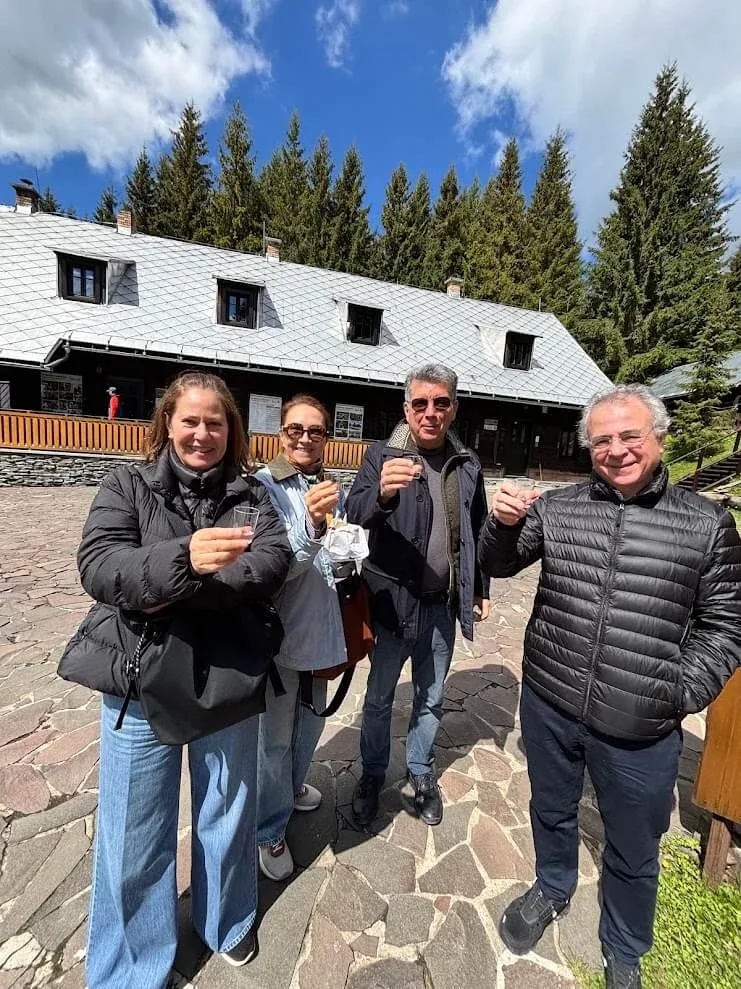 Four guests raising small glasses in a welcome toast outside a timber mountain lodge in Orava.