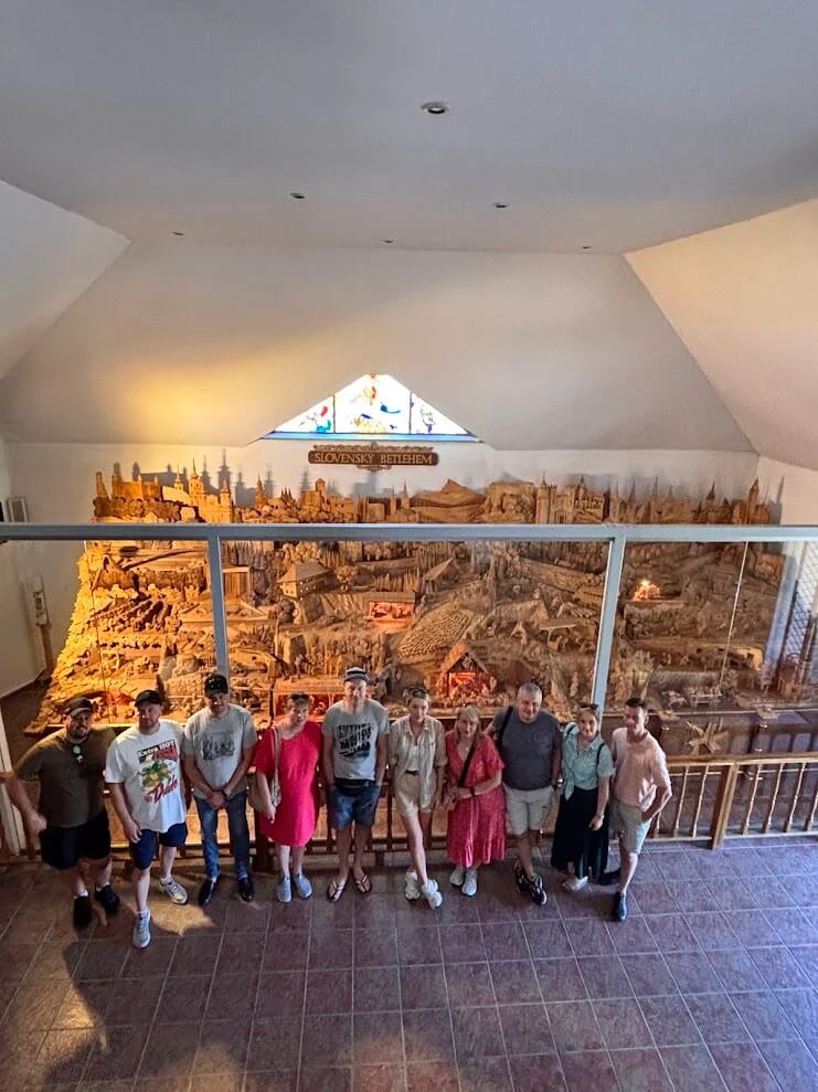 A group in front of the Slovak Bethlehem at Rajecká Lesná, a carved wooden panorama of Slovak landmarks and nativity scenes.