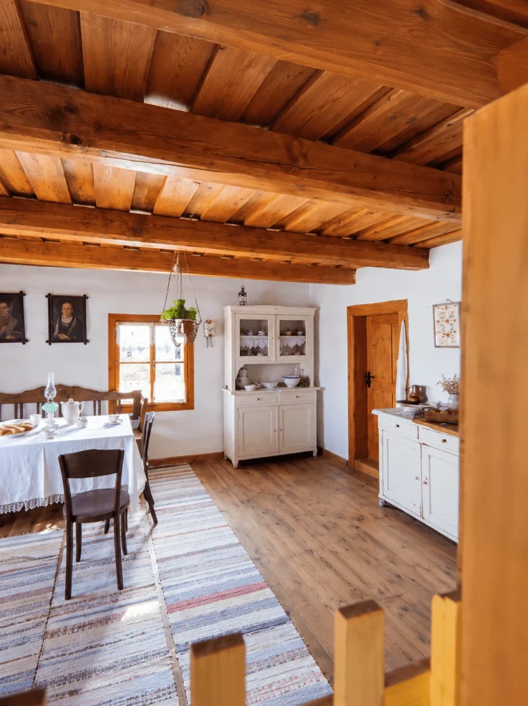 The interior of a traditional Slovak wooden cottage, with a laid table, a painted dresser and a timber ceiling.