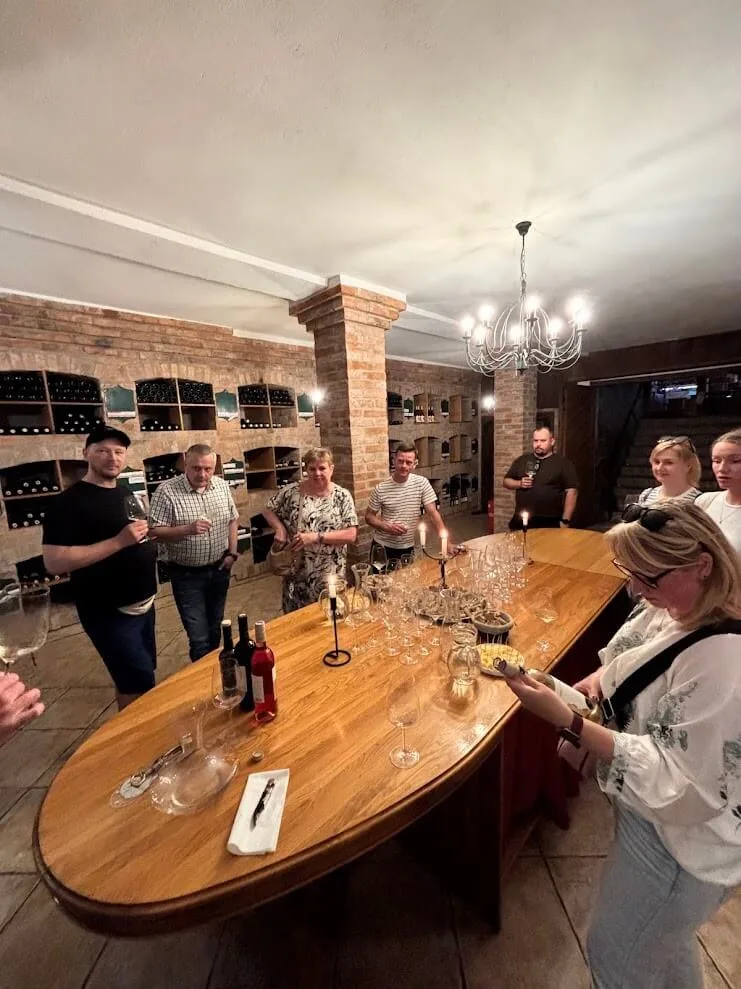 A group at a wine tasting in a brick vaulted cellar in the Small Carpathians, with glasses and bottles set out along a long wooden table.