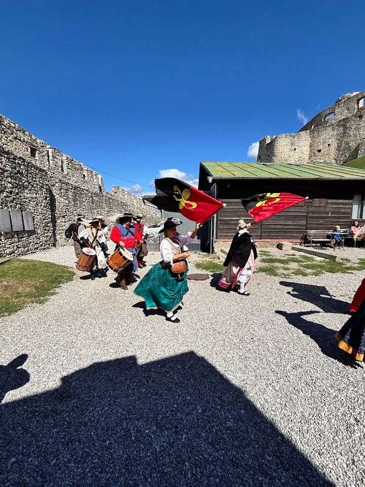 Musicians and dancers in historical costume with drums and heraldic flags in the courtyard of Spiš Castle.