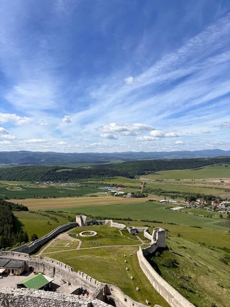 The lower courtyard of Spiš Castle seen from the keep, with the Spiš plain and distant hills beyond its long curtain walls.