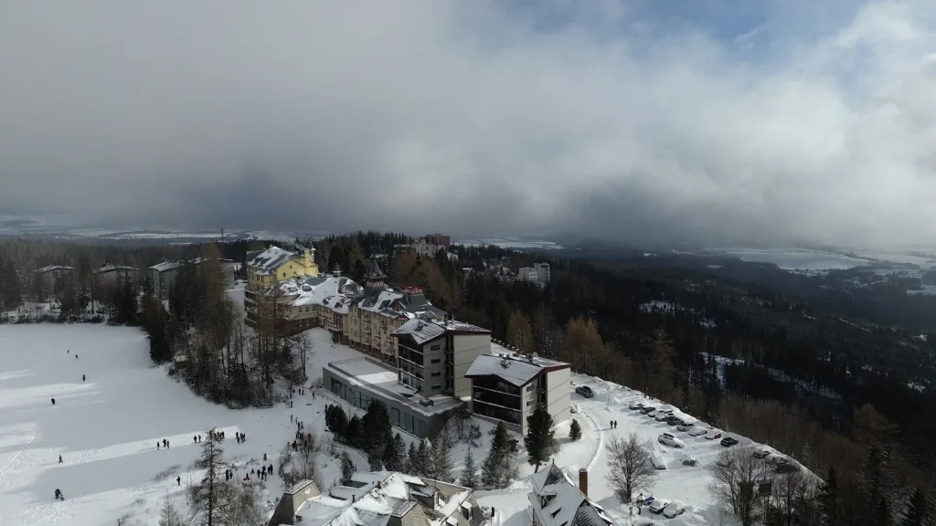 An aerial view of Štrbské Pleso in winter, its hotels and the frozen lake under low cloud.