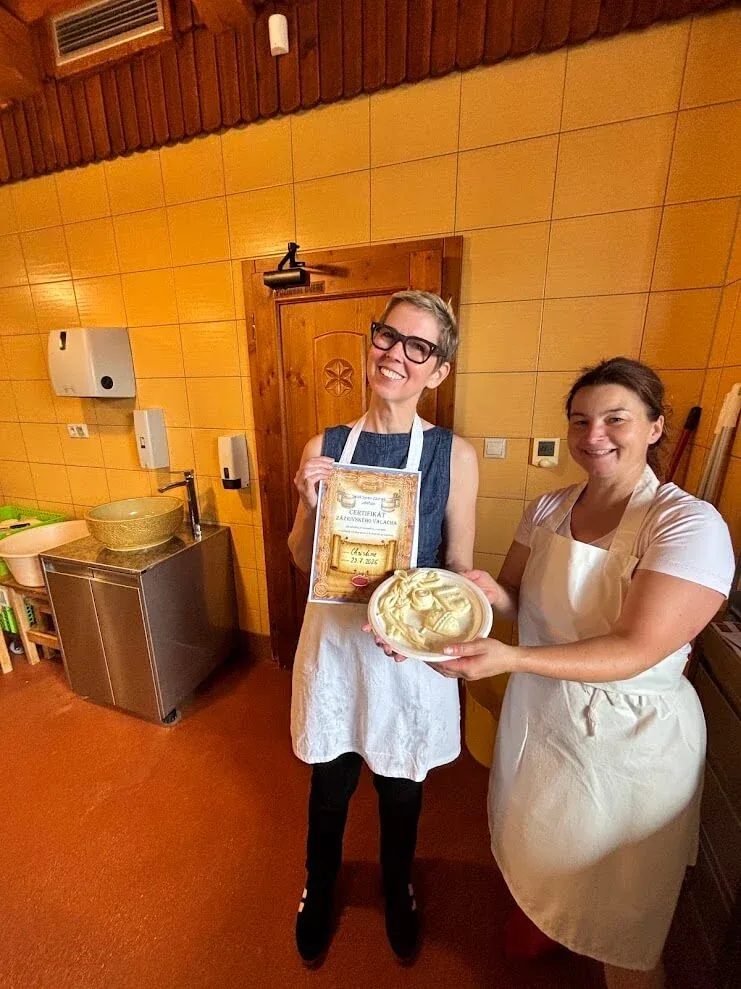 A visitor and a cheesemaker holding a certificate and a moulded round of traditional Slovak sheep cheese in a small dairy near Terchová.