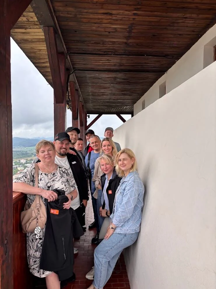 A tour group on the covered wooden gallery high on Trenčín Castle, with the town and hills visible beyond.