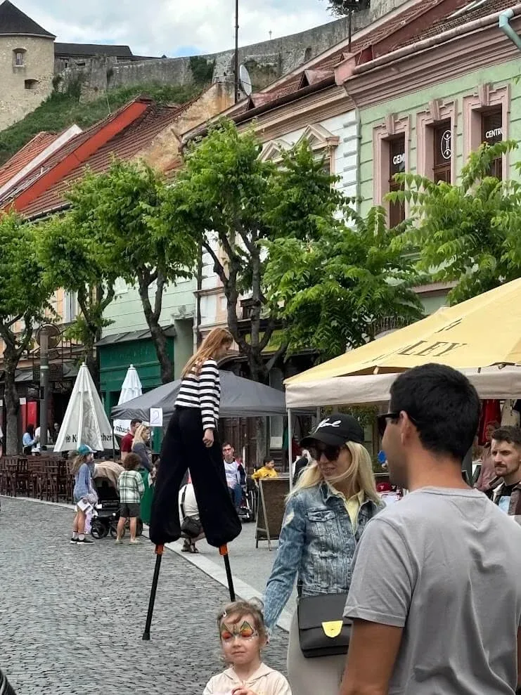 A stilt walker performing on a cobbled street in Trenčín during a festival, with the castle walls on the hill behind.