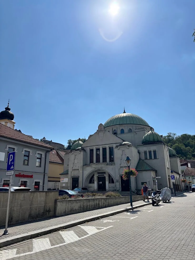 The domed synagogue in Trenčín, its green copper roofs and arched entrance under a bright summer sky.