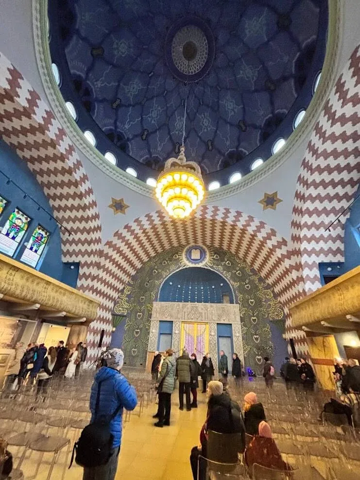 Visitors inside the restored synagogue in Trenčín, beneath its painted blue dome and zigzag-striped arches.