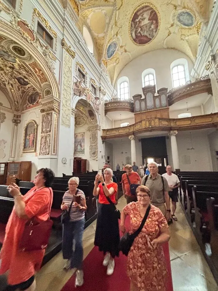 A tour group walking down the nave of St John the Baptist Cathedral in Trnava, looking up at its frescoed vault.