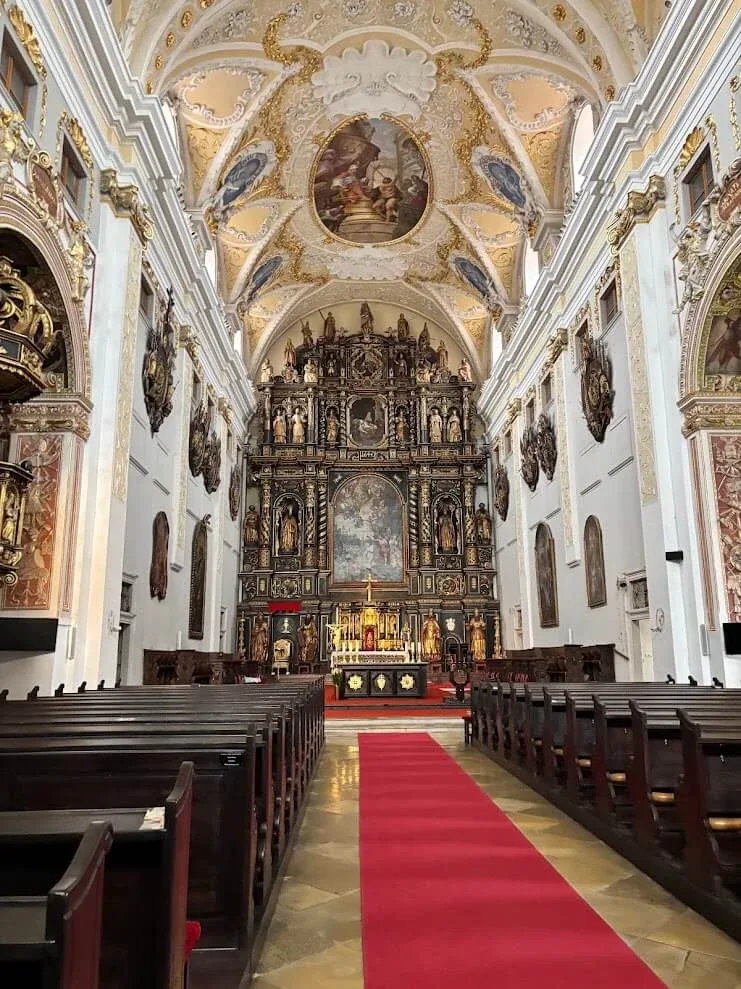 The vast carved wooden high altar of St John the Baptist Cathedral in Trnava, one of the largest in Europe, at the end of a red-carpeted nave.