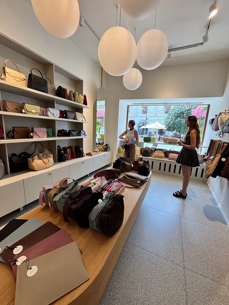 A bright leather-goods shop in Trnava, bags displayed on pale shelves under round pendant lamps.