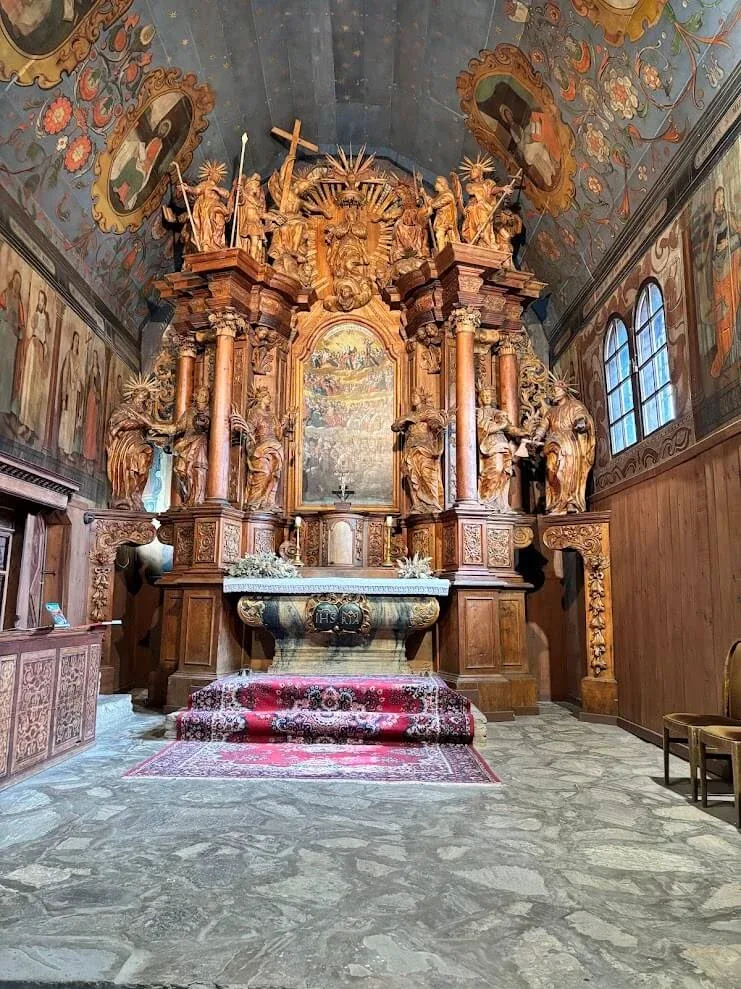 The carved and gilded baroque altar inside the wooden church at Tvrdošín, beneath a painted timber ceiling.