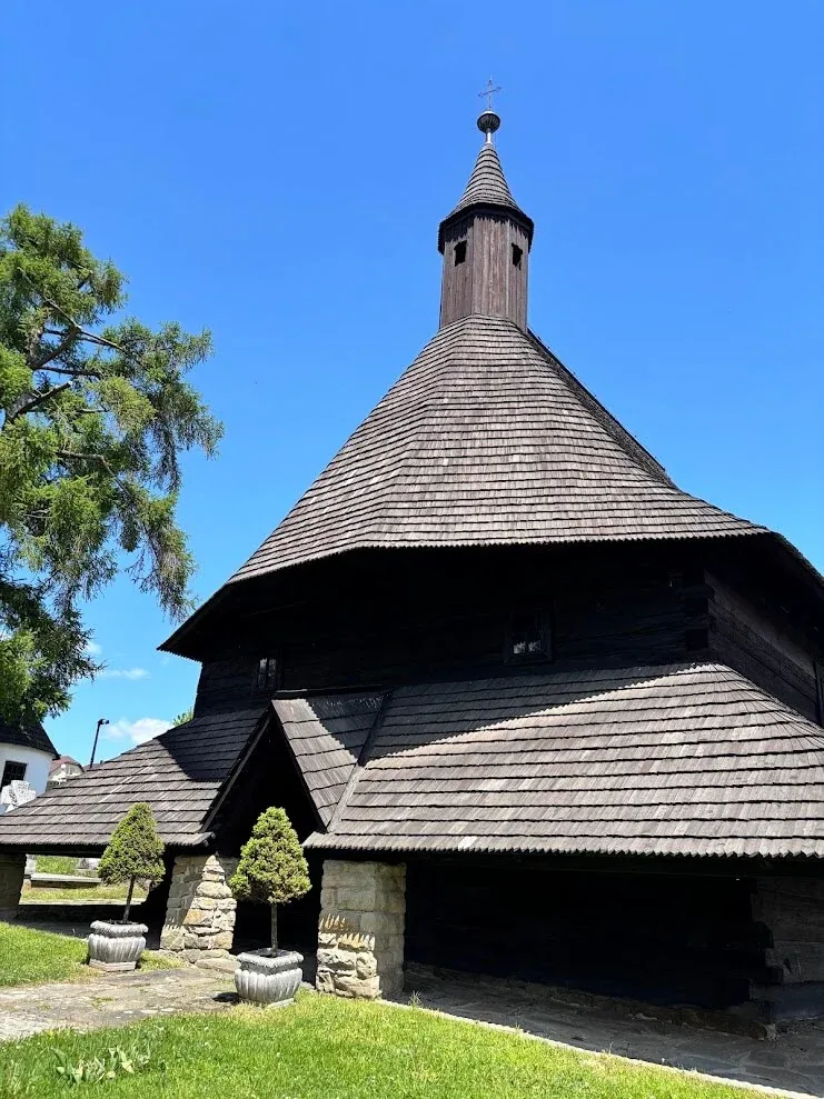 The UNESCO-listed wooden church at Tvrdošín, its dark shingled roofs and slender tower against a clear blue sky.