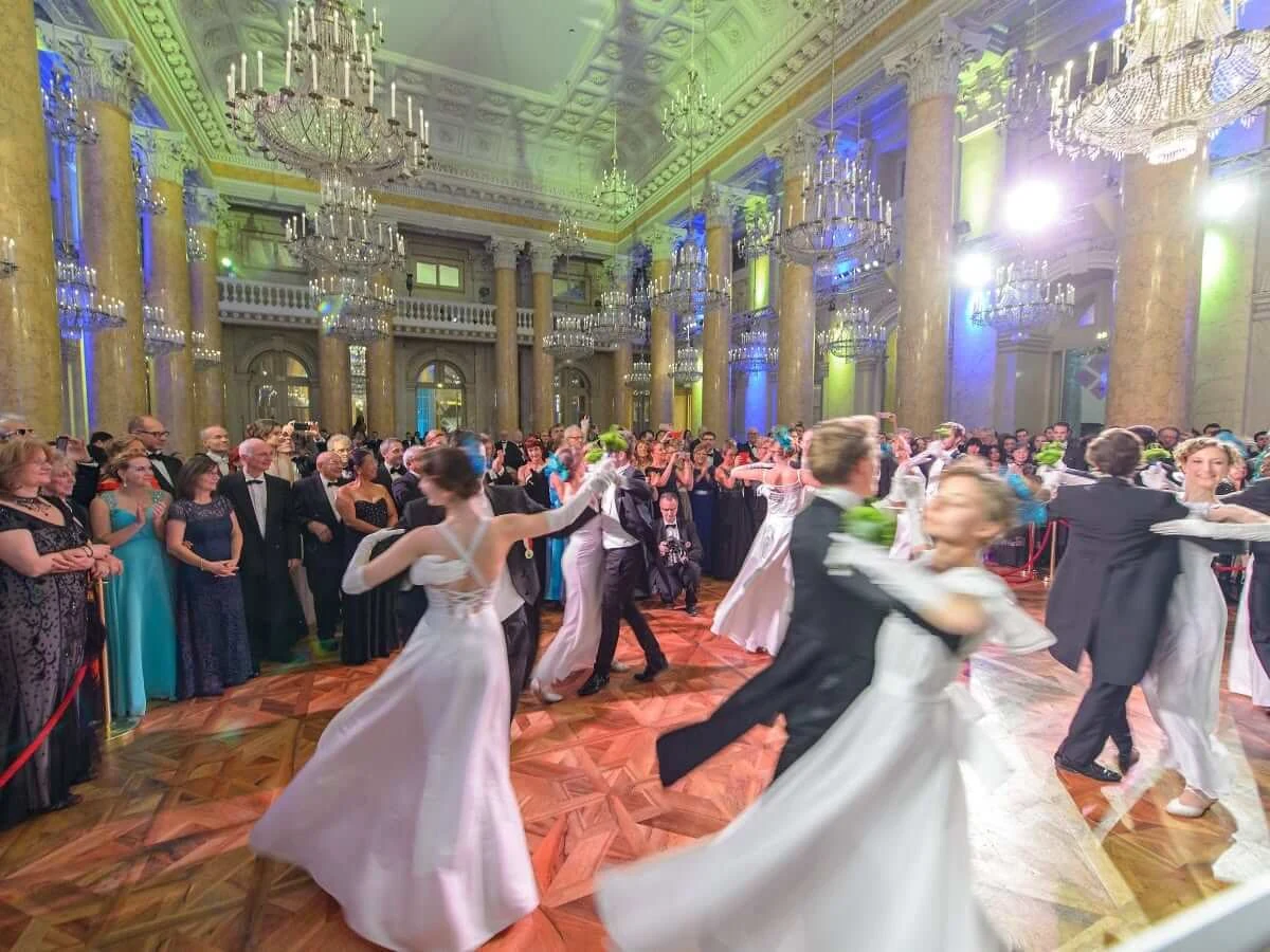 Des débutantes en robes blanches valsant avec leurs cavaliers lors d'un bal viennois, sous des lustres en cristal dans une salle de bal à colonnes.